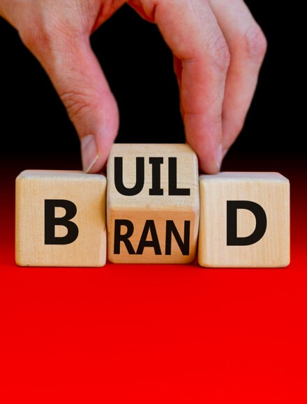 Build your brand symbol. Businessman turns wooden cubes and changes the word ‘build’ to ‘brand’. Beautiful orange background. Build your brand and business concept. Copy space. Build your brand symbol. Businessman turns wooden cubes and changes the word 'build' to 'brand'. Beautiful orange background. Build your brand and business concept. Copy space.